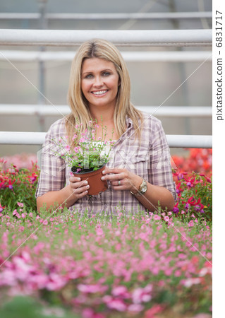 Woman holding a flower while standing in greenhouse Woman holding a flower while standing in greenhouse 6831717