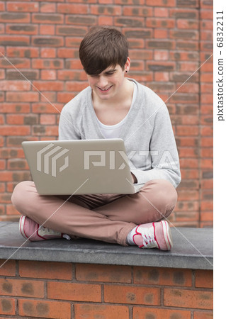 Man sitting cross legged and using laptop outside 6832211
