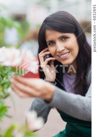 Smiling florist touching a flower and making a call Smiling florist touching a flower and making a call 6832691