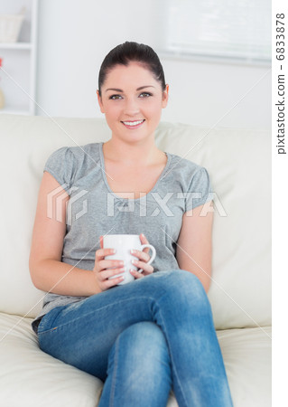 Smiling woman sitting on the couch and holding a mug 6833878
