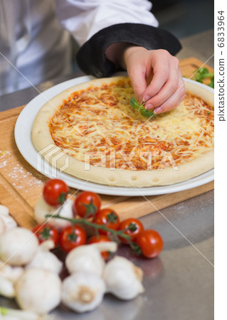 Pizza being garnished with basil leaf 6833964