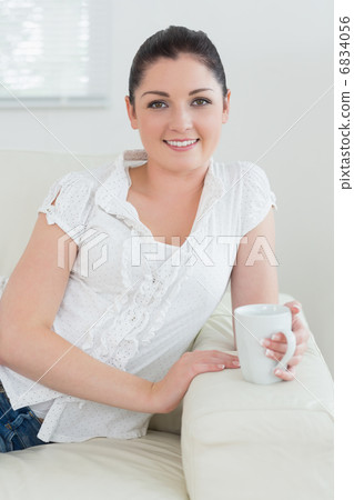 Woman holding a cup while sitting on the couch Woman holding a cup while sitting on the couch 6834056