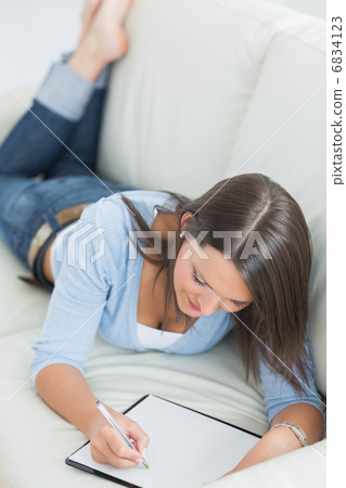 Smiling woman lying on sofa and writing 6834123