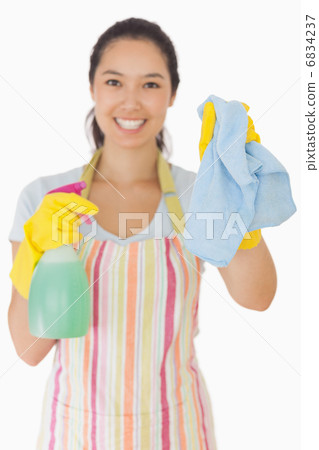 Smiling woman holding up rag and spray bottle 6834237