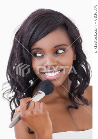 Woman holding makeup brush to her face Woman holding makeup brush to her face 6836370