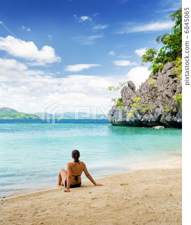 Young beautiful woman is sitting on sand by the sea Young beautiful woman is sitting on sand by the sea 6845065