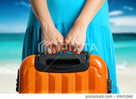 Woman in blue dress holds orange suitcase in hands on the beach Woman in blue dress holds orange suitcase in hands on the beach 6845066