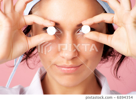 Closeup portrait of young nurse showing pills over eyes Closeup portrait of young nurse showing pills over eyes 6894354