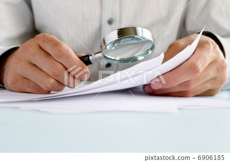 Businessman looking through a magnifying glass to documents. Businessman looking through a magnifying glass to documents. 6906185