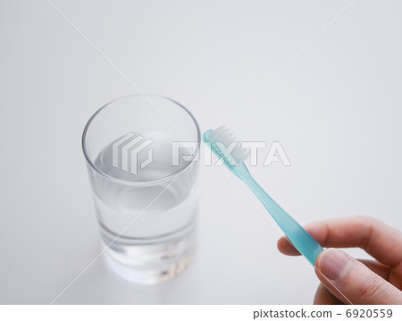 用玻璃杯裡的水潤濕牙刷。 用玻璃杯裡的水潤濕牙刷。 6920559