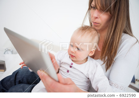 Serious woman holding her baby while using a tablet pc Serious woman holding her baby while using a tablet pc 6922590