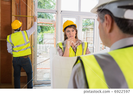 Woman and architect talking while man is measuring wooden frame Woman and architect talking while man is measuring wooden frame 6922597