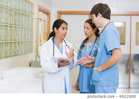 Female doctor talking to a male and a female nurse in a hallway Female doctor talking to a male and a female nurse in a hallway 6922800