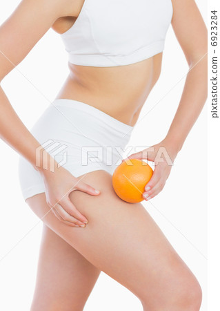 Fit woman squeezing fat on thigh as she holds orange Fit woman squeezing fat on thigh as she holds orange 6923284