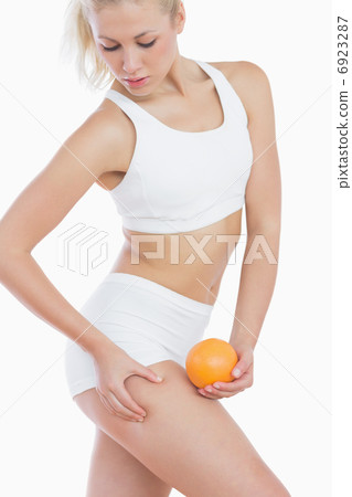Woman checking out fat on thigh as she holds orange Woman checking out fat on thigh as she holds orange 6923287