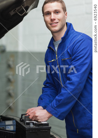 Happy male mechanic with car battery 6923540