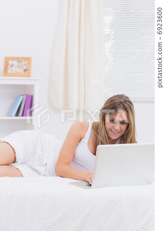 Cheerful woman lying on her bed with a laptop Cheerful woman lying on her bed with a laptop 6923600