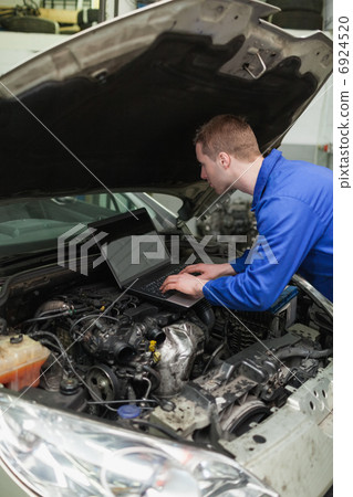 Mechanic using laptop on car engine 6924520