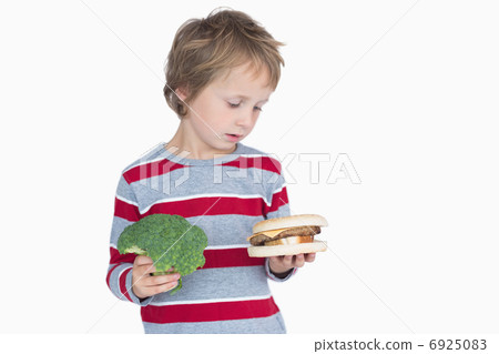 Young boy holding broccoli and burger Young boy holding broccoli and burger 6925083