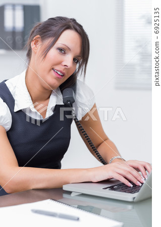 Business woman using landline phone and laptop at desk Business woman using landline phone and laptop at desk 6925135