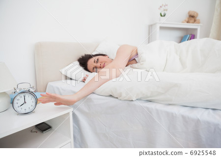 Sleepy woman extending hand to alarm clock Sleepy woman extending hand to alarm clock 6925548