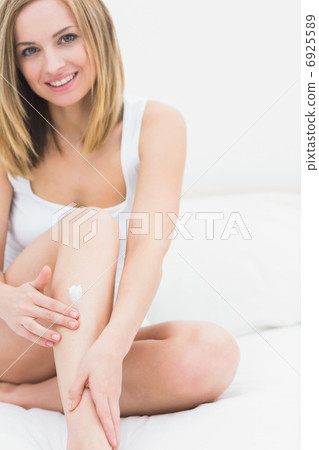 Woman applying cream on leg while sitting on bed 6925589