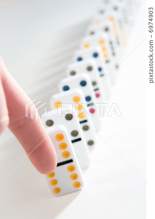 Finger about to knock over line of dominoes 6974903