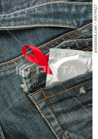 Condom in jeans pocket with red awareness ribbon Condom in jeans pocket with red awareness ribbon 6974927
