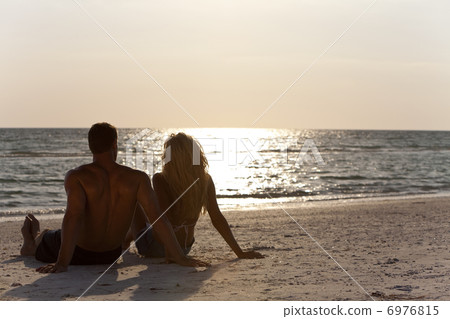 Young Man and Woman Couple Sitting on Beach At Sunset Young Man and Woman Couple Sitting on Beach At Sunset 6976815