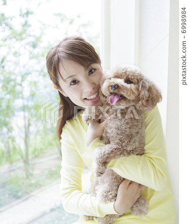 A woman holding a toy poodle and sitting at the window 6998984