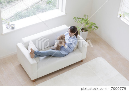 A woman sitting on a sofa and holding a toy poodle 7000779