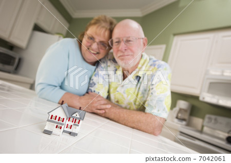 Senior Adult Couple Gazing Over Small Model Home on Counter 7042061