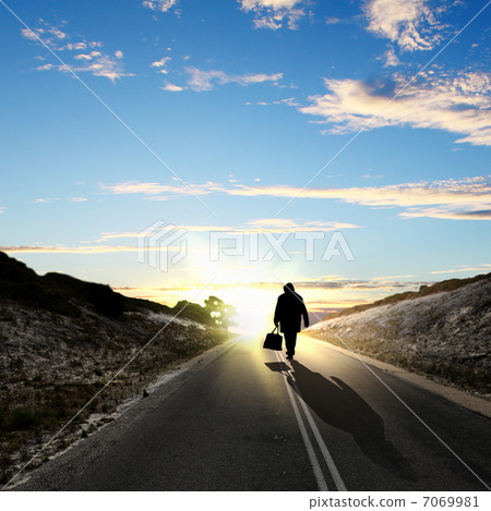 Man walking away at dawn along road 7069981