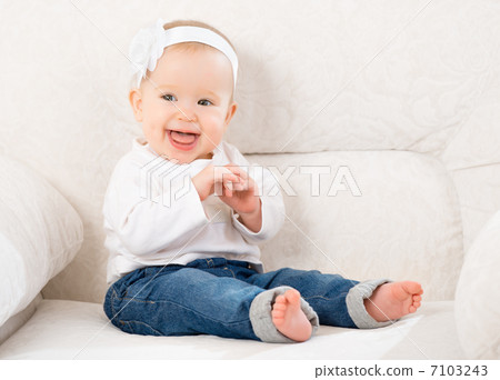 happy little baby girl laughing and sitting on a sofa in jeans 7103243