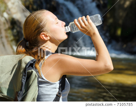 Young woman drinks water by waterfall Young woman drinks water by waterfall 7105785