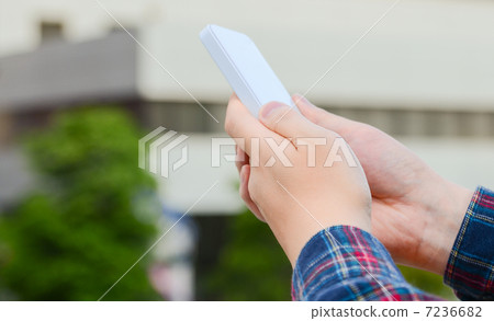 A hand operating a smartphone and a cityscape in the background. A hand operating a smartphone and a cityscape in the background. 7236682