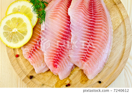 Fillets tilapia with lemon on a round board Fillets tilapia with lemon on a round board 7240612