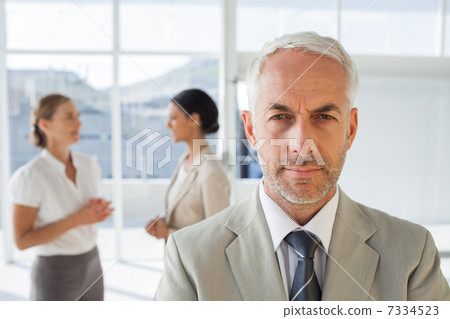 Serious businessman standing while colleague are discussing toge 7334523
