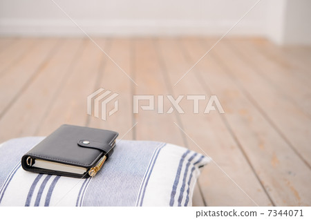A personal organizer and pen placed on a cushion, in a brightly lit room. 7344071