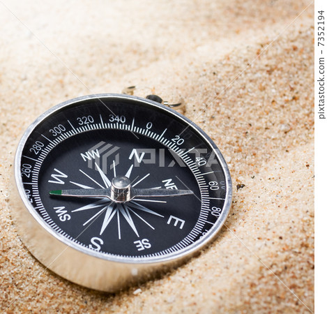 compass in the sand lit by the rays of the sun 7352194