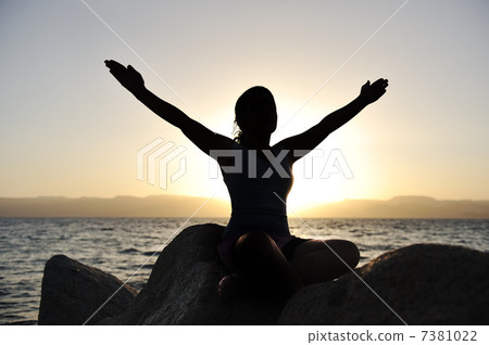 Silhouette of a beatiful female meditating on a rock by the sea 7381022