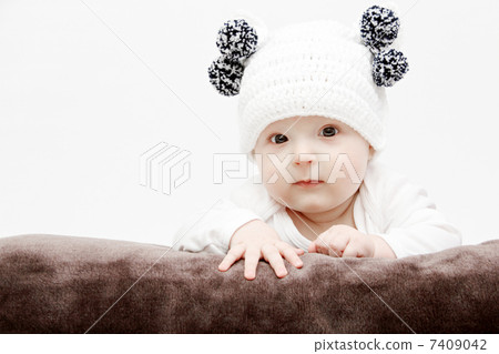 baby in white hat lies on bed 7409042