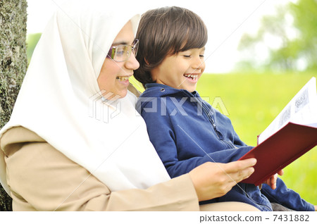 Mother Muslim and her son in the nature, reading together Mother Muslim and her son in the nature, reading together 7431882