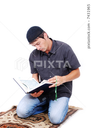 Muslim man is holding holly book Qoran and praying on traditiona 7431965