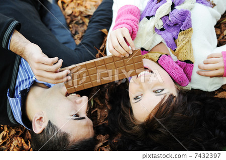 Young beauty girl and her boyfriend eating together chocolate in nature together , fall scene on ground Young beauty girl and her boyfriend eating together chocolate in nature together , fall scene on ground 7432397