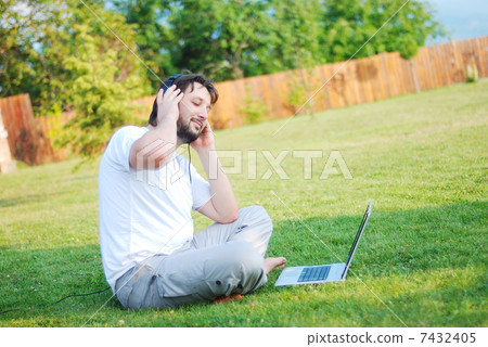 Happy young man on green meadow with laptop 7432405