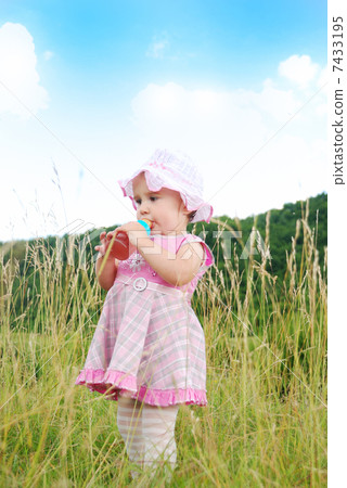 Baby girl standing in nature and drinking milk from bottle Baby girl standing in nature and drinking milk from bottle 7433195