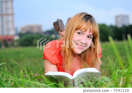 Young smiling woman lying on meadow with book 7541120