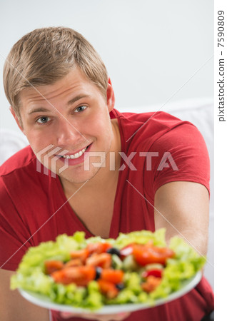 Young man eating vegetarian salad with appetite Young man eating vegetarian salad with appetite 7590809
