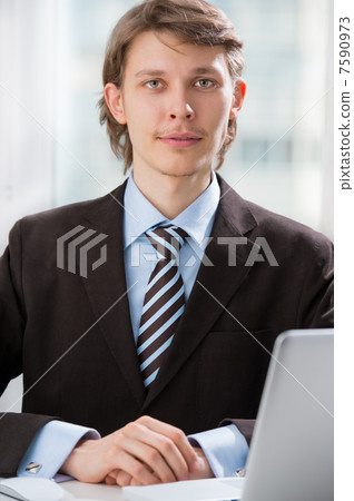 Happy executive sitting in front of laptop with arms on table Happy executive sitting in front of laptop with arms on table 7590973